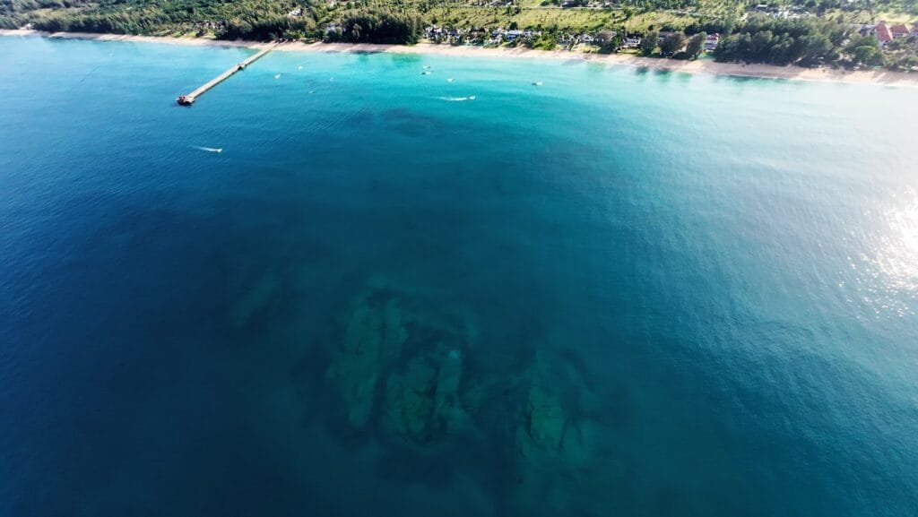  Aerial view of the expansive coral reef system stretching across the beachfront of Twin Villas Natai, a luxury private villa on Natai Beach near Phuket, ideal for snorkeling and marine exploration.
