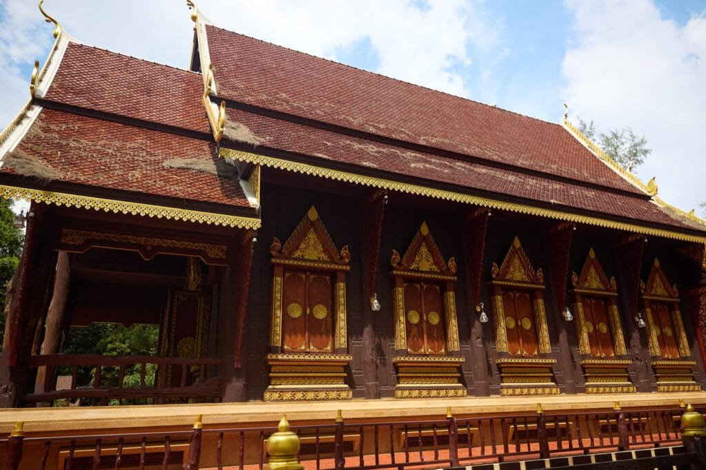 Exterior view of Thettharamnawa Temple (Wat Tha Sai) near Natai Beach, showcasing traditional Thai wooden architecture with ornate gold detailing and a sloping tiled roof, a cultural stop for families exploring local temples in Phang Nga.
