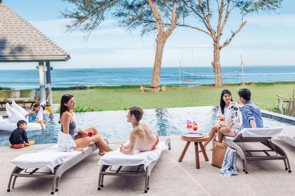 Families enjoying a relaxing time by the beachfront infinity pool at Twin Villas Natai, with ocean views and a serene villa setting.