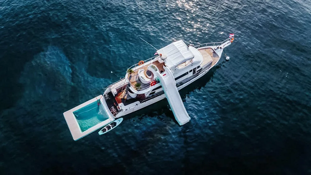 Top Family Activities In and Around Natai Beach | Twin Villas Natai Top-down view of a luxury motor yacht equipped with an inflatable water slide and a sea pool, offering safety-first fun for children in calm waters.