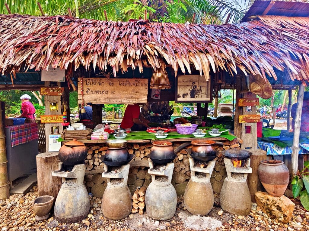 Authentic Southern Thai cooking at Long Lae Sunday Market, featuring traditional clay pots over charcoal braziers at a rustic market stall.
