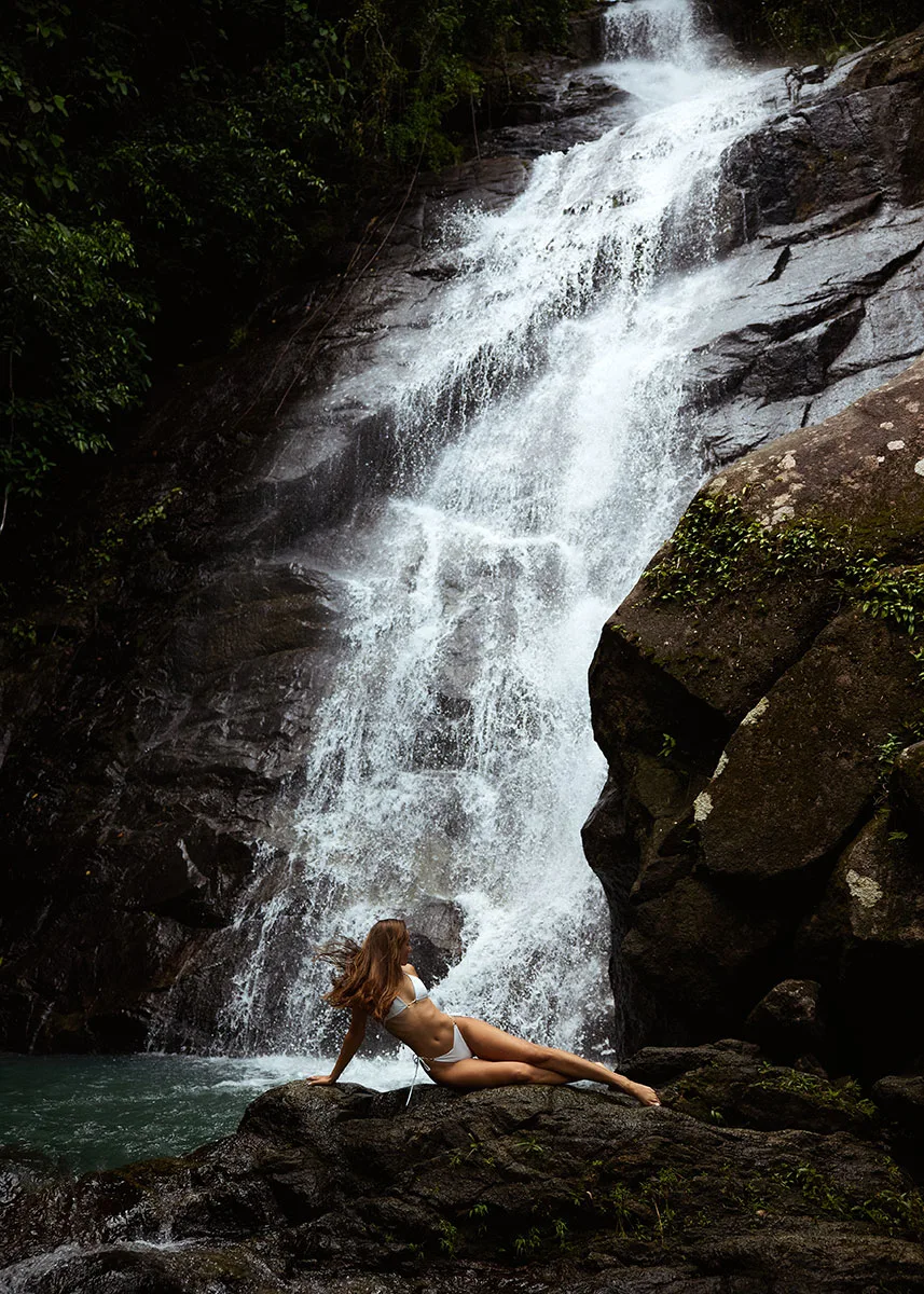 Top Family Activities In and Around Natai Beach | Twin Villas Natai A young woman in a white bikini sitting on rocks at the base of the majestic Phu Pha Sawan (Tong Sung) Waterfall in Phang-Nga.