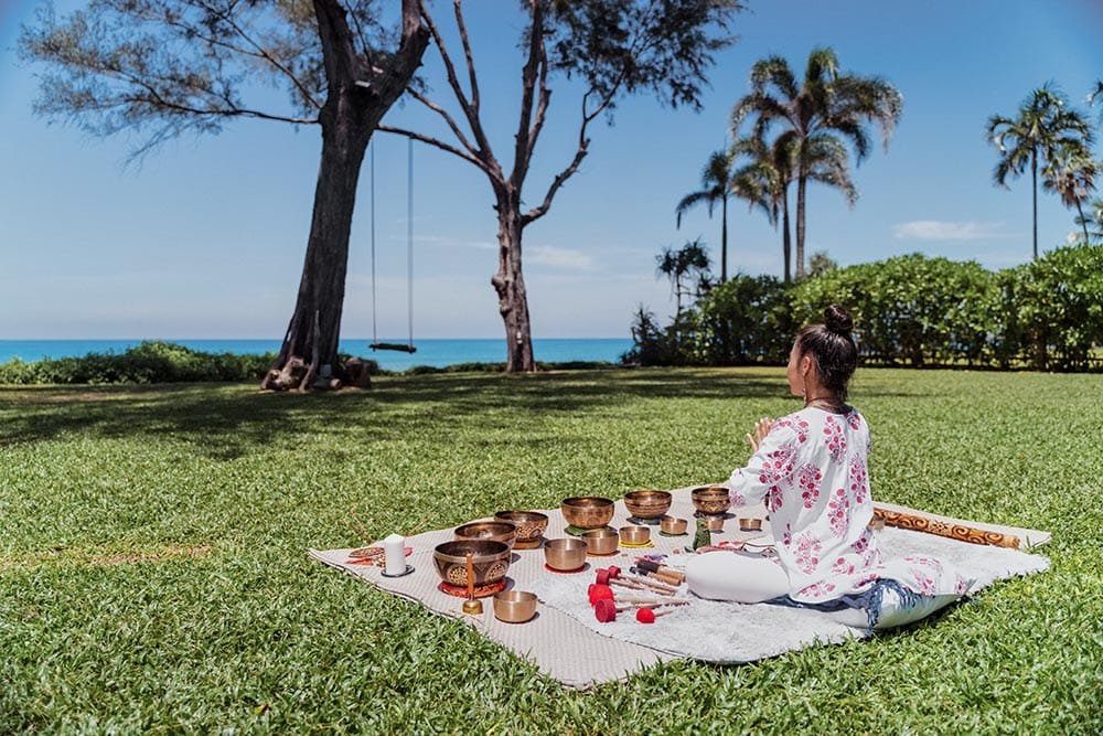 Retreat Villas Near Phuket – A Private Beachfront Wellness Sanctuary at Twin Villas Natai | Twin Villas Natai Sound therapy session with singing bowls on a beachfront lawn overlooking the ocean during a private wellness retreat.