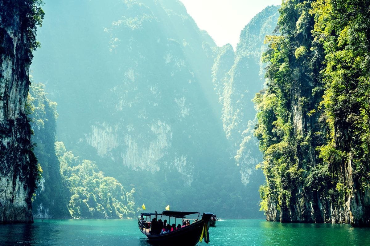 Discover Phang Nga Attractions: The Best Day Trips from Natai Beach, Thailand | Twin Villas Natai Longtail boats navigating between limestone cliffs on Cheow Lan Lake in Khao Sok National Park, Thailand.